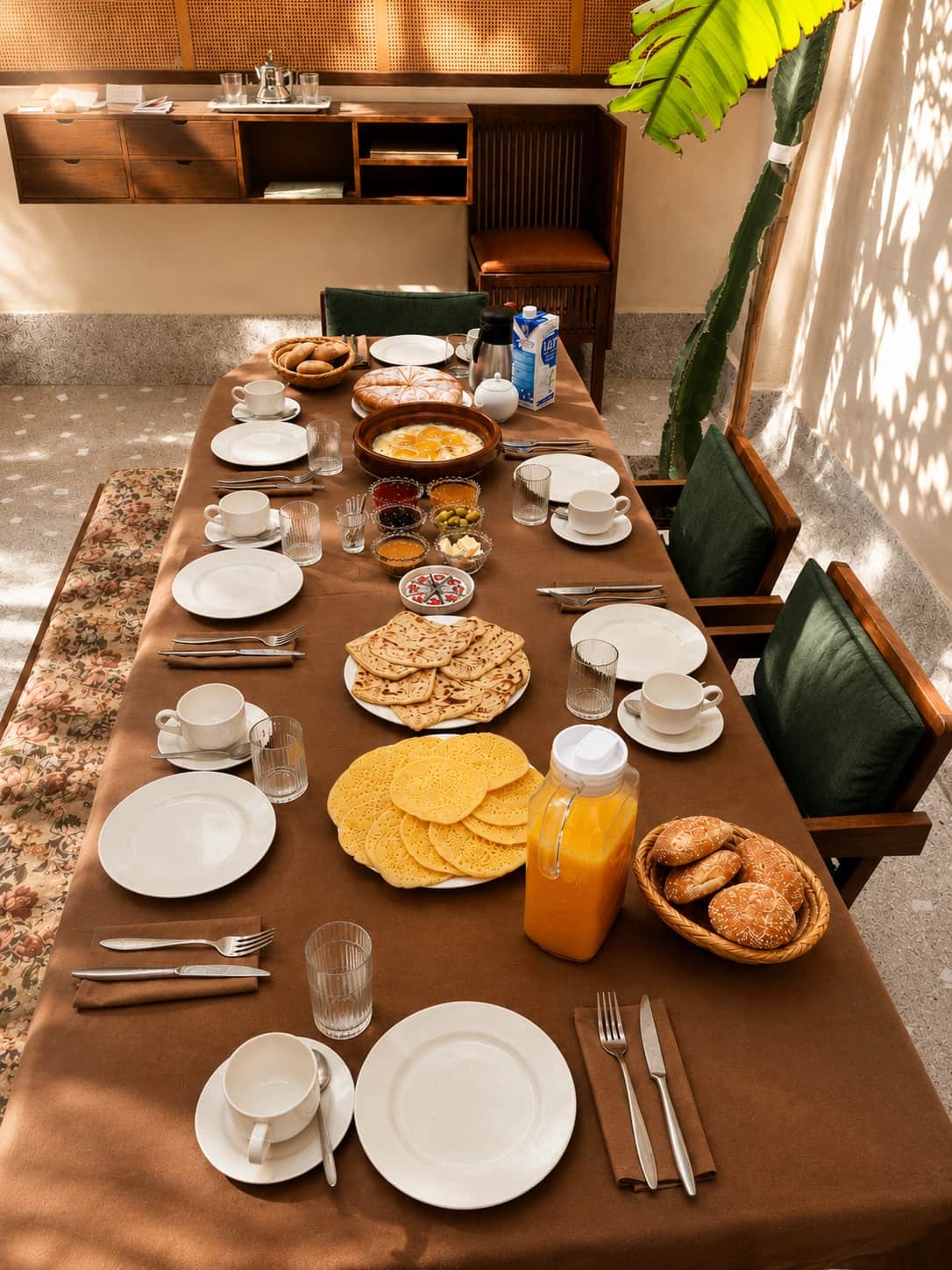 La grande table dressée pour le petit déjeuner : msemen, baghrir, œufs, olives, confitures et pain du quartier. Pris dans le patio, à votre rythme.