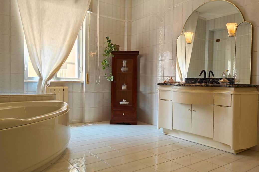 Ampio bagno con vasca angolare, doppio lavabo in marmo e arredi eleganti. Un’oasi di relax perfetta dopo una giornata tra mare e cultura a Siracusa.