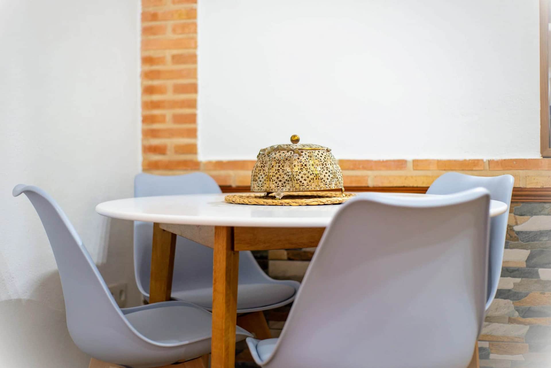 Comedor acogedor con mesa redonda blanca, cuatro sillas modernas grises y pared decorada con ladrillo y piedra