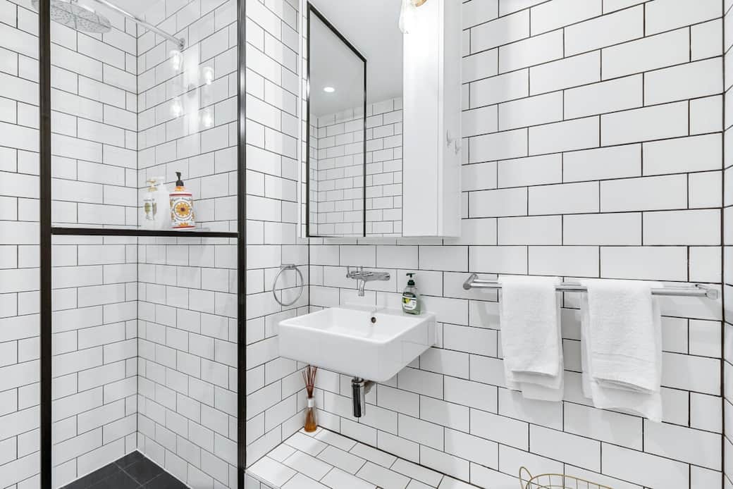 Experience the luxury of our bathroom, featuring a glass-enclosed shower that adds a touch of elegance. The white brick tiles and modern fixtures create a bright, airy space. Enjoy a refreshing shower and the convenience of well-placed towels.