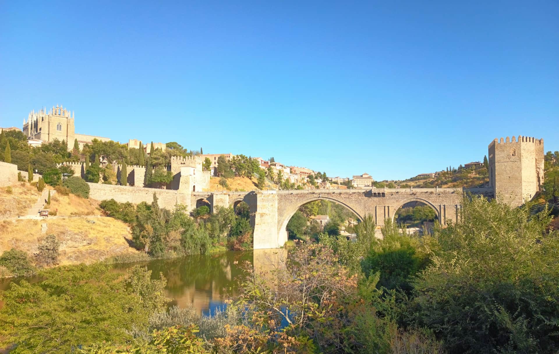 Alojamiento rural cerca de Puy du Fou - La Casita de Ale, escapada cultural en Toledo Puente de San Martín en Toledo, rodeado de vegetación y arquitectura histórica bajo un cielo despejado