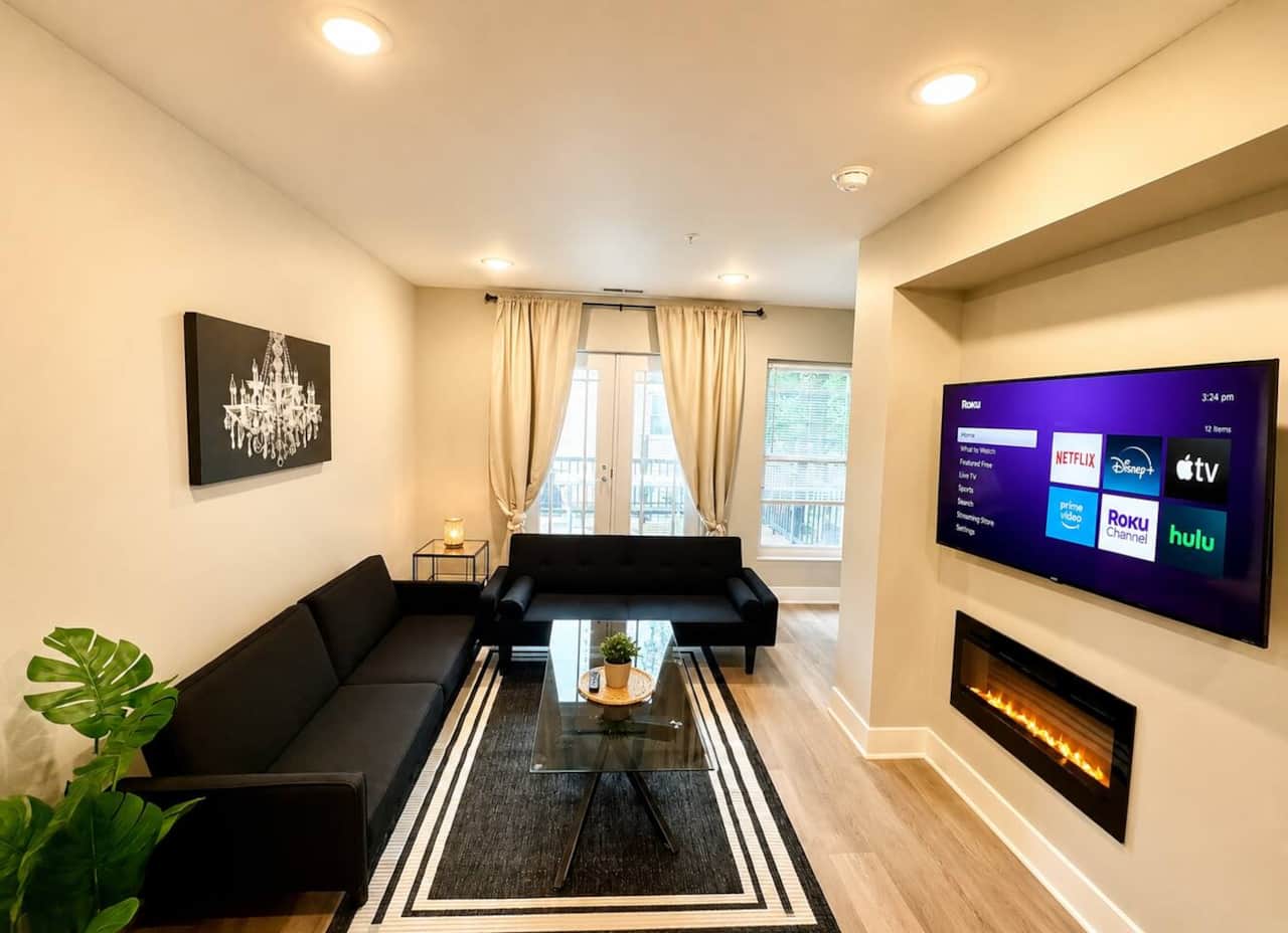 Bright, modern living room featuring two comfortable futon sofa beds, a large Roku TV, electric fireplace, and direct walkout access to the deck. A cozy space to relax, stream your favorite shows, or enjoy fresh air right outside.