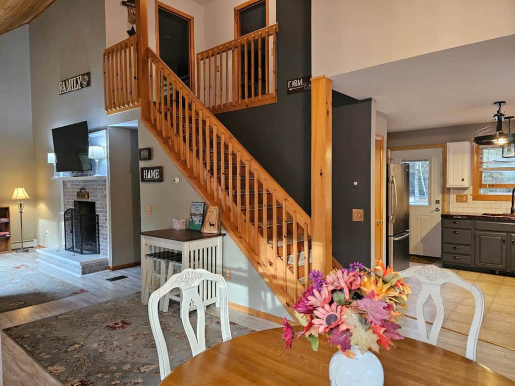 Enjoy the open layout with a charming staircase leading upstairs, a cozy fireplace and TV in the living room, and a stylish kitchen nearby. The bright dining area with floral centerpiece ties the spaces together for family gatherings.