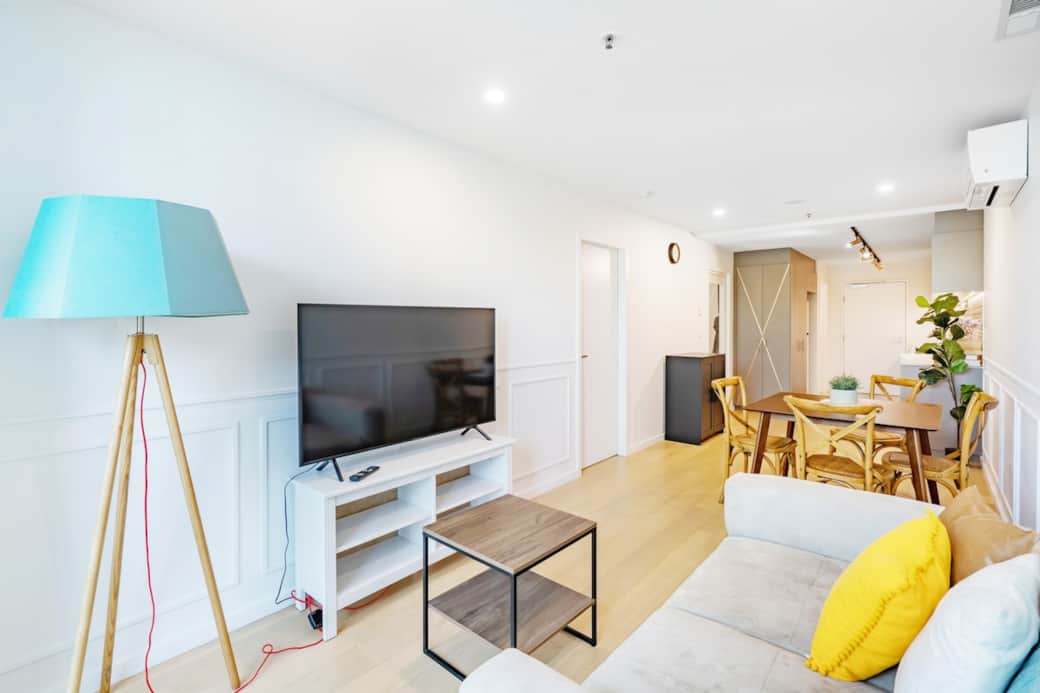 The living room is a cozy retreat, featuring a plush sofa and a stylish coffee table. The floor lamp with a blue shade adds a pop of color, while the flat-screen TV offers entertainment. A welcoming space to unwind after a day of exploration.