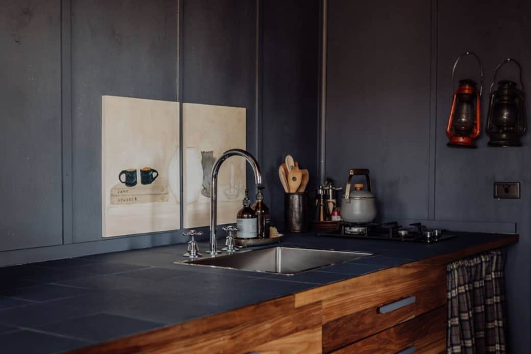 Side view of kitchen with two gas-burner stove, bar fridge and deep sink. Fully stocked with dishes, pots and pans and mug and glassware.