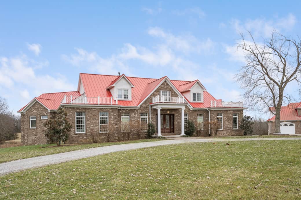 Exterior of spacious brick home with eye-catching red roof, welcoming front porch & scenic setting Exterior of spacious brick home with eye-catching red roof, welcoming front porch & scenic setting