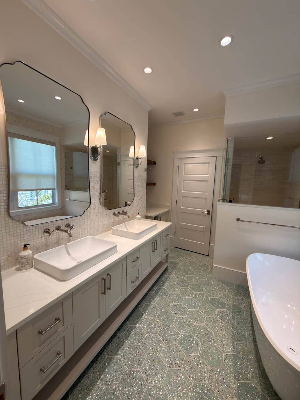 A spacious, spa-like en-suite bath featuring a walk-in shower, soaking tub, and his and hers vanity. Finished in a refined coastal-modern style, it offers a bright, luxurious setting designed for comfort, relaxation, and privacy.