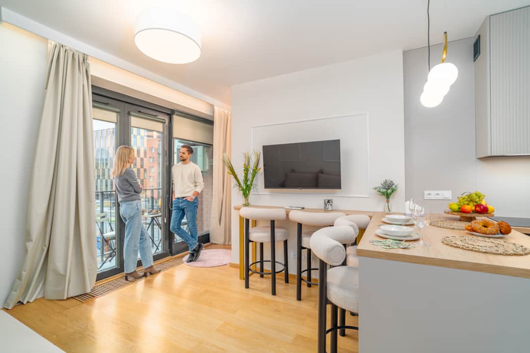 Jasny salon z aneksem kuchennym i balkonem, urządzony w nowoczesnym, eleganckim stylu.