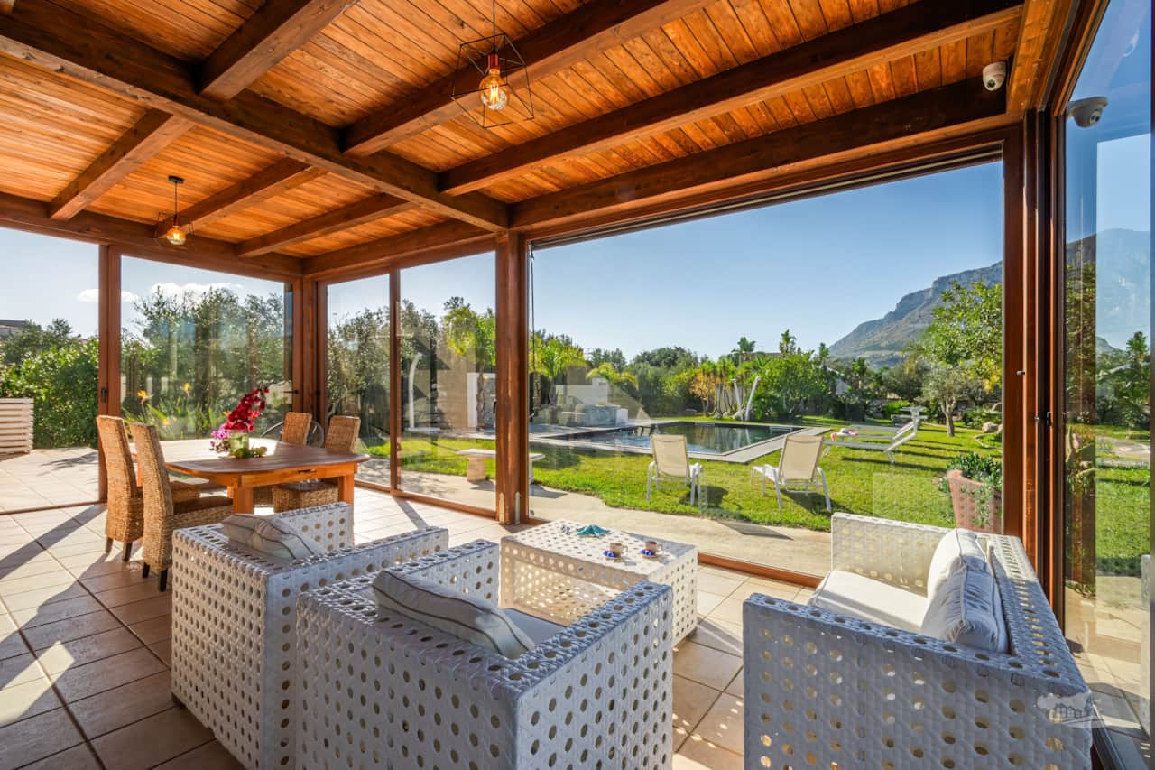 Bright and inviting, this patio with wooden beams overlooks a serene pool and lush greenery.