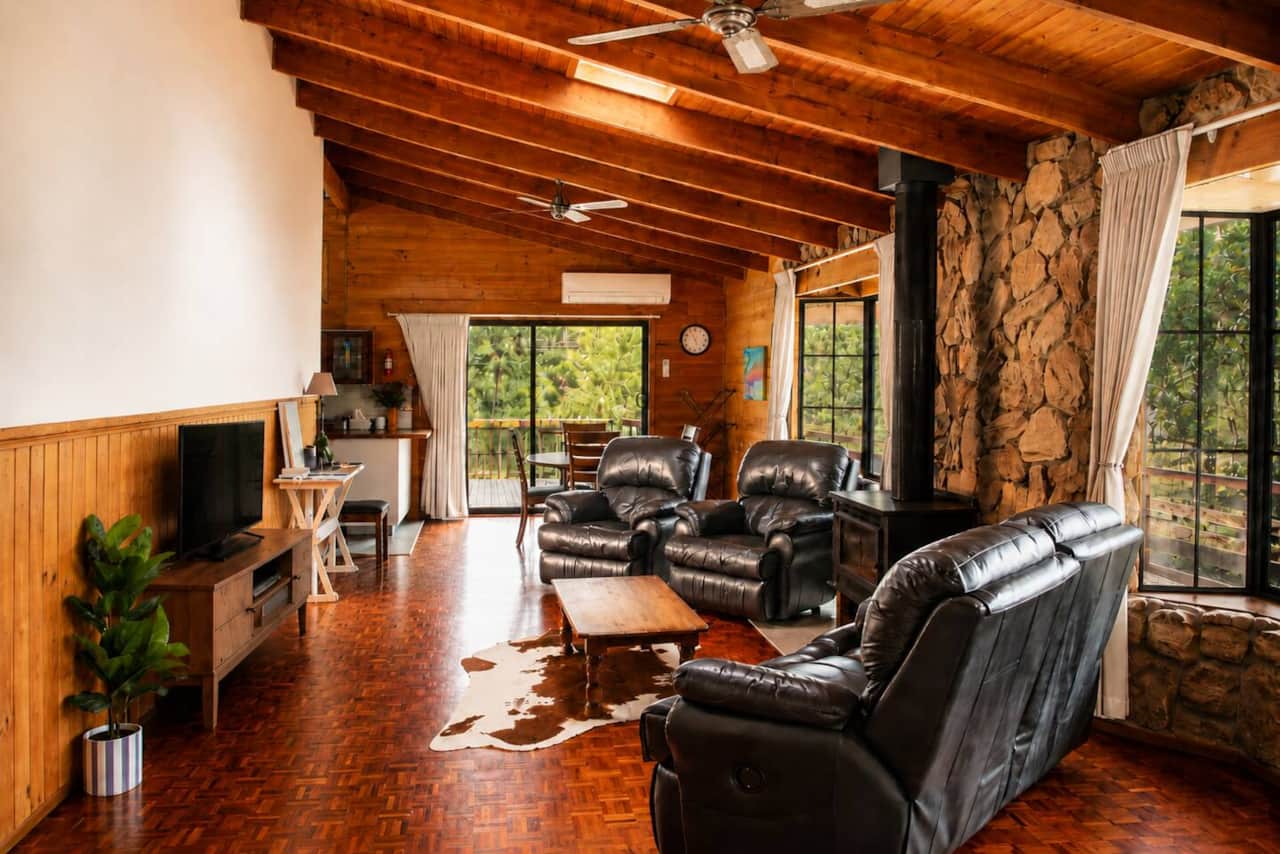 A warm, character-filled living space with leather seating, timber-lined ceilings, a wood-burning fireplace and leafy garden outlook.