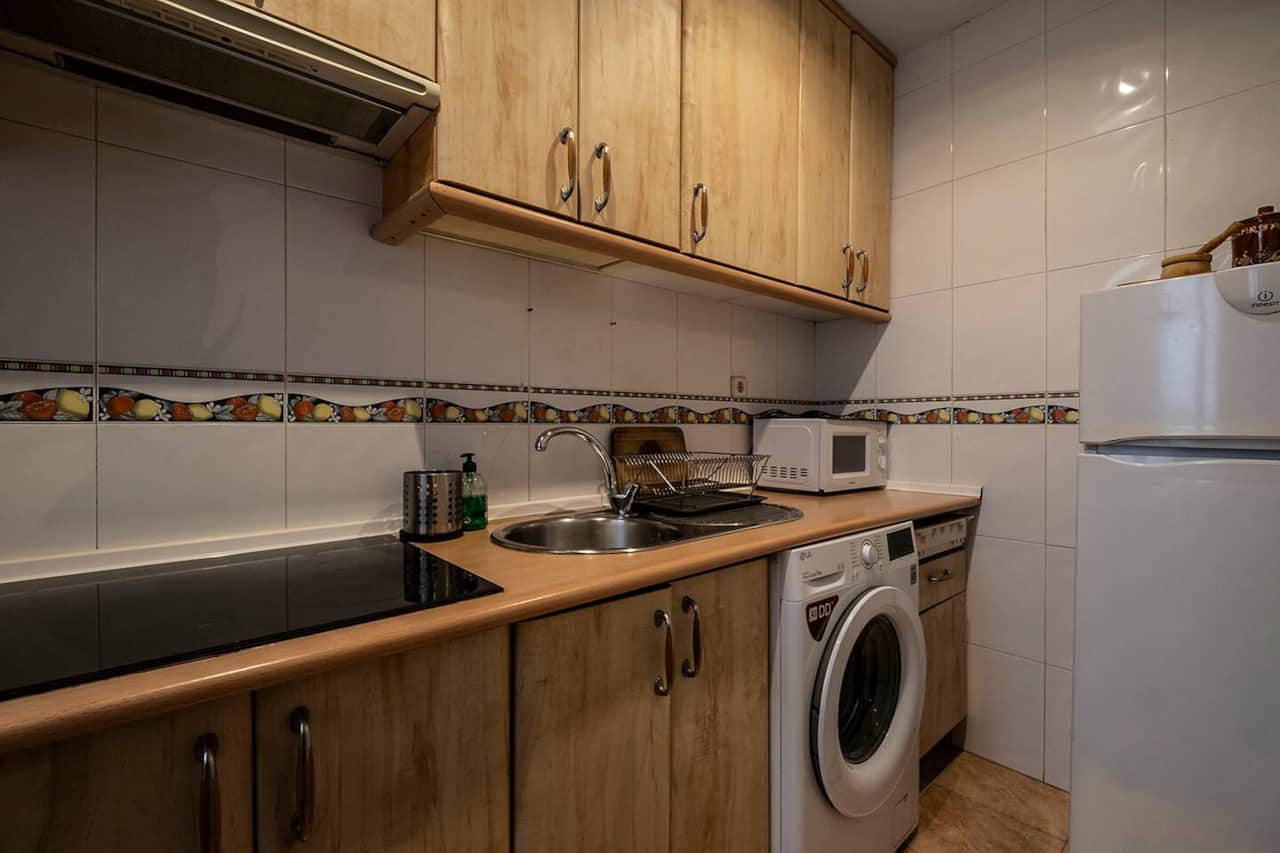 Cocina con vitrocerámica, lavadora y armarios de madera