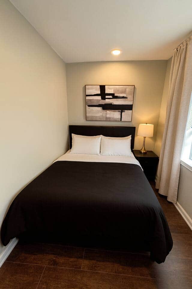 Small Modern queen bedroom with a 50-inch TV, black duvet, white pillows, closet, and warm hardwood floors — clean, cozy, and perfect for Airbnb guests.