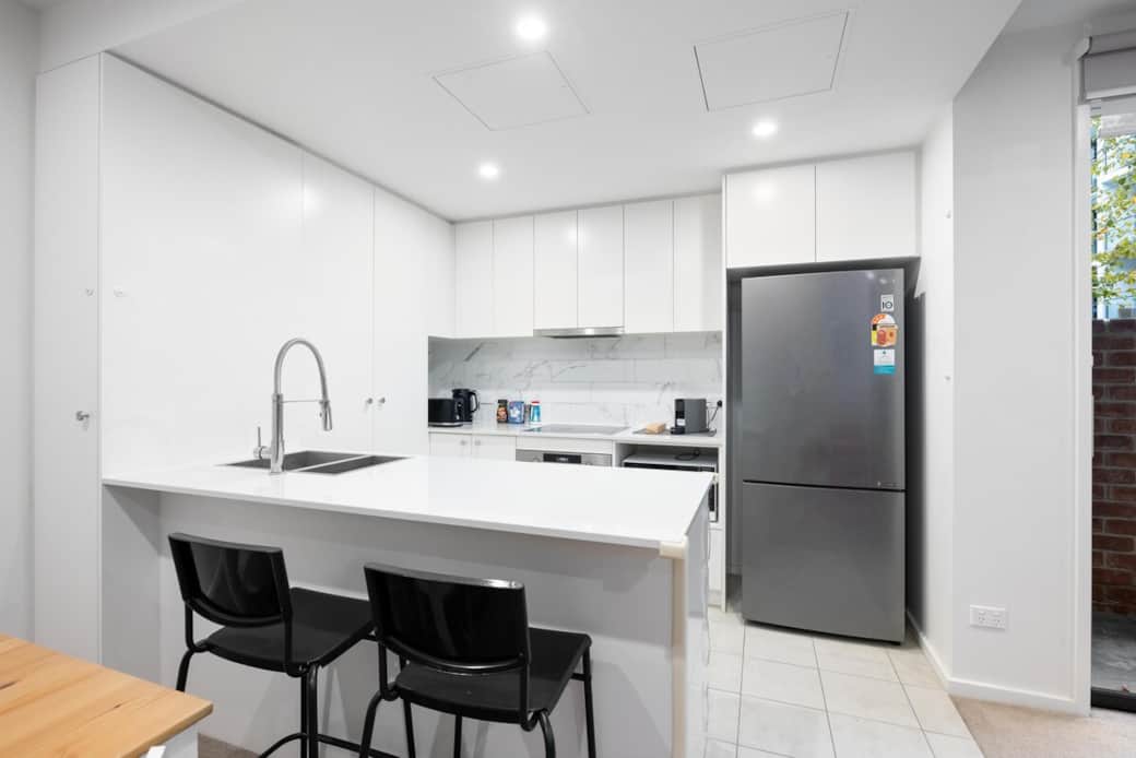 This modern kitchen is a chef's delight with a sleek design. It features a large island with a sink and bar stools, perfect for casual dining. The stainless steel fridge and oven are ready for your culinary adventures, creating a welcoming space.