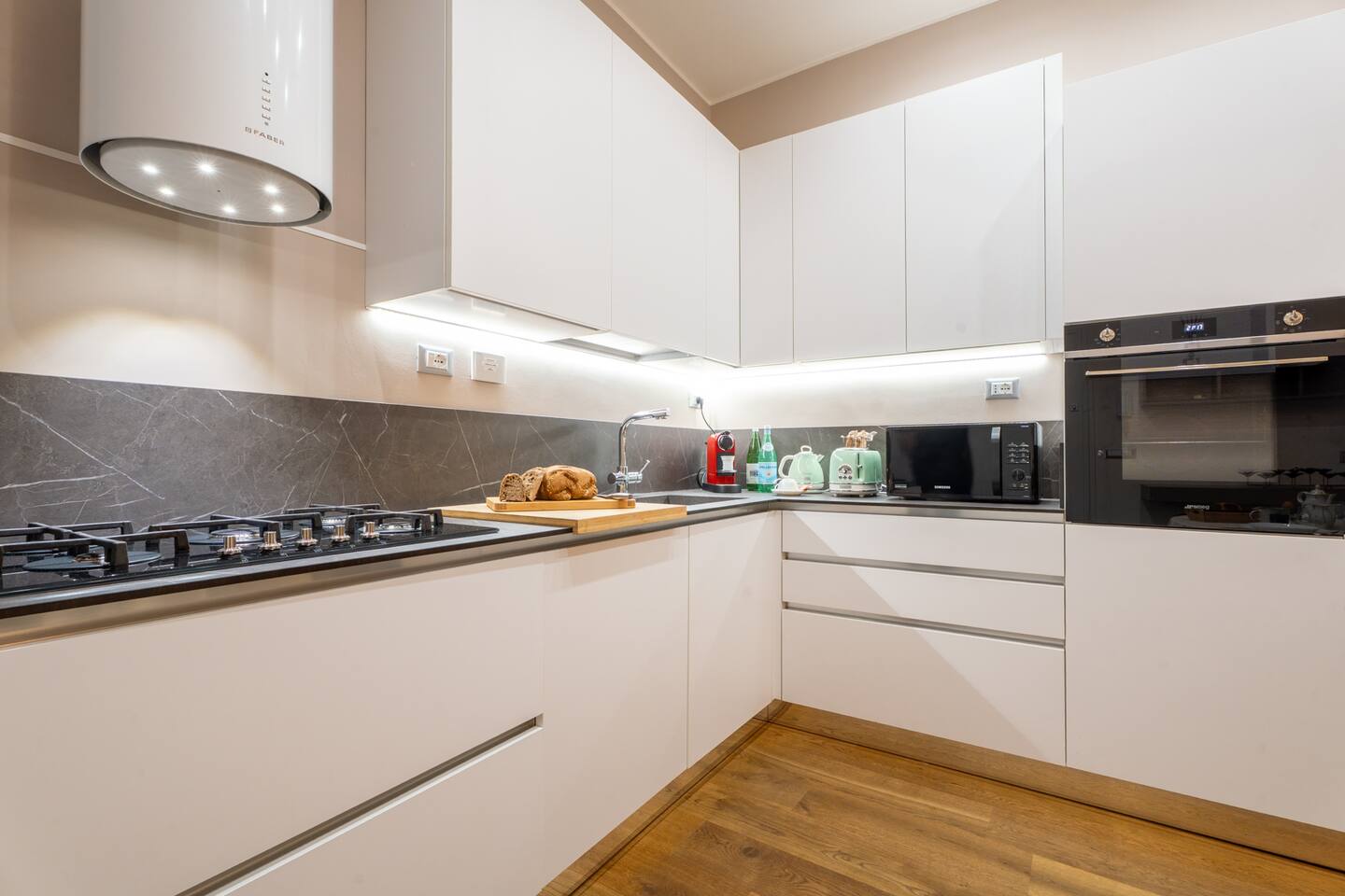 Cucina moderna e attrezzata con tutti gli elettrodomestici Smeg. Illuminazione LED sotto i pensili per un'ottima visibilità del piano di lavoro. Piano cottura 5 fuochi a gas metano, forno multifunzione, lavastoviglie, frigorifero combinato.