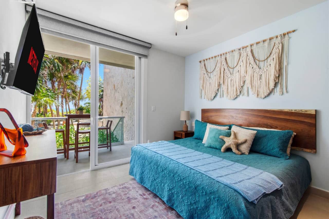 Wake up to Caribbean Sea views from the primary bedroom, featuring a king-size bed, Smart TV, air conditioning, ceiling fan, wardrobe, and room-darkening shades, plus direct access to the private balcony, hot tub, and garden.