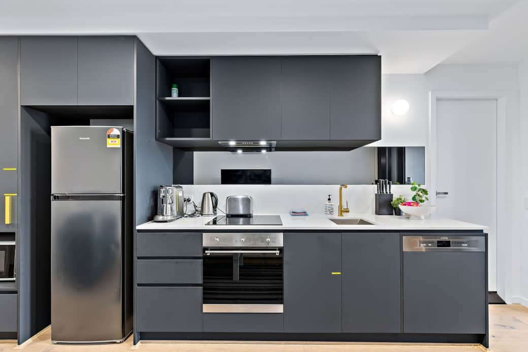 Experience the joy of cooking in this modern kitchen, where sleek gray cabinetry meets stainless steel appliances. The gas stove and oven are ready for your culinary creations, while the large refrigerator ensures ample storage for fresh ingredients.