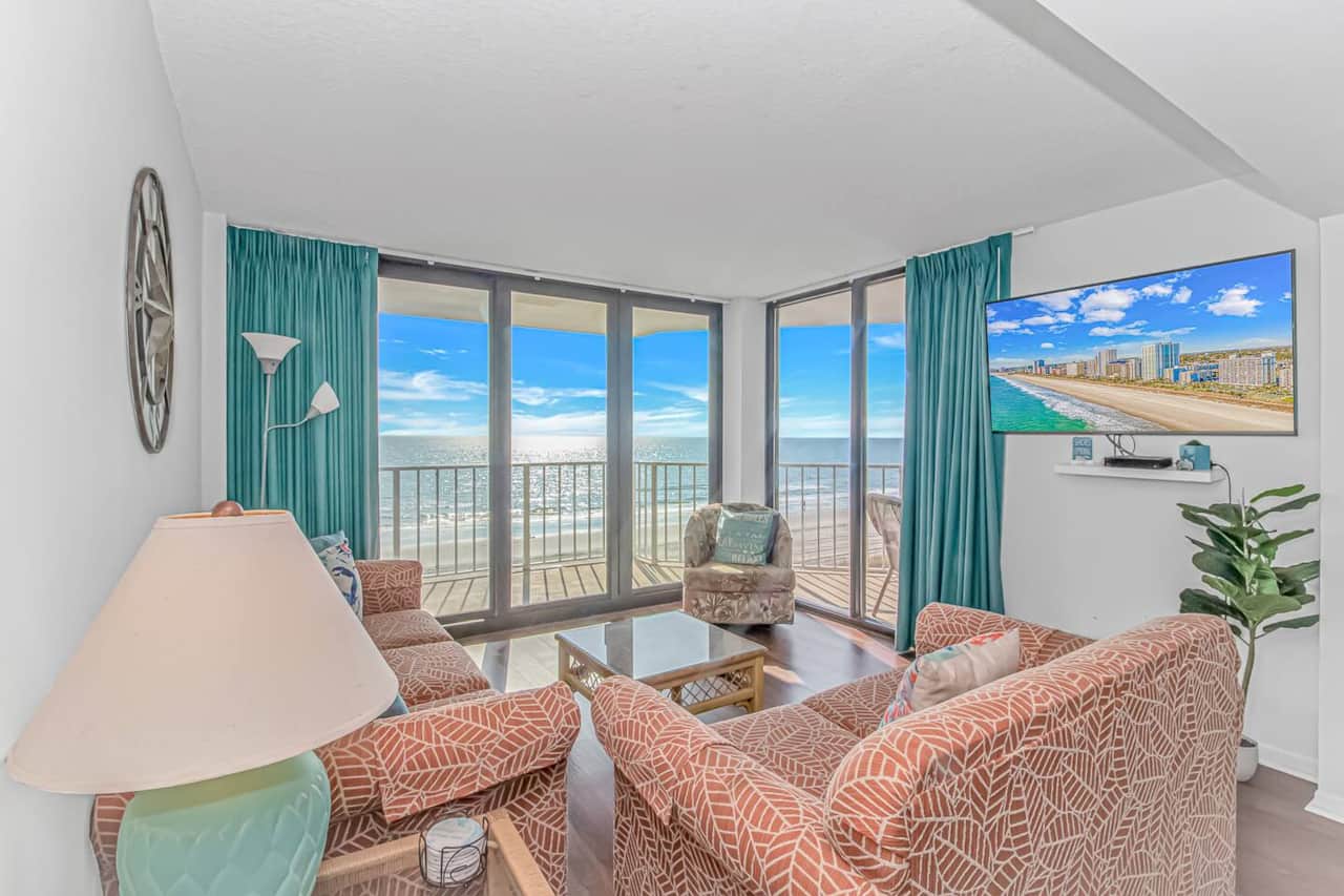 Bright and inviting living room featuring wrap-around windows, coastal décor, and breathtaking views of the shoreline.