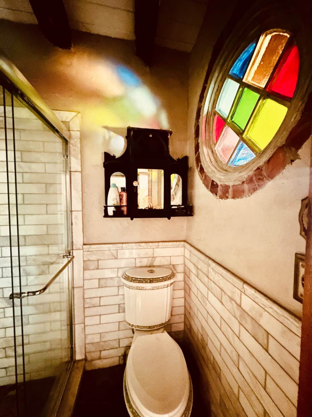 Our ode to marble bathroom features a toilet that looks like a teacup, a rainhead shower with an additional handheld faucet, a restored stained glass church window, pastel pebbled floor, and a walnut Victorian medicine cabinet.