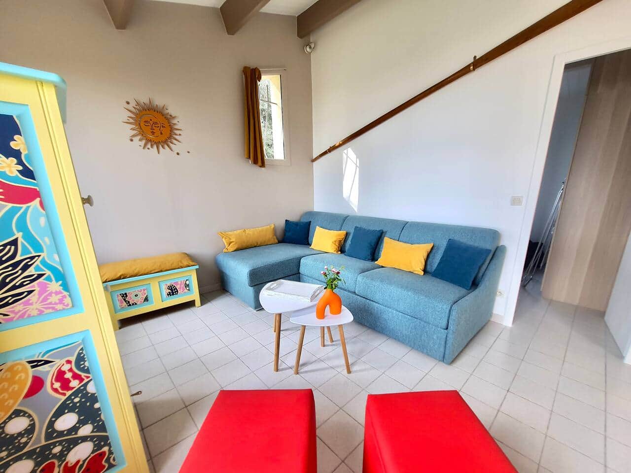 Un coin salon cosy et lumineux, parfait pour se détendre en fin de journée. Le canapé d’angle invite à la détente, avec une touche de couleur apportée par les coussins et le mobilier d’appoint.