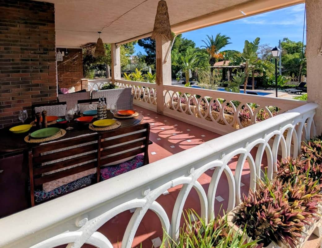 Groot overdekt terras met eettafel en uitzicht op tuin en zwembad