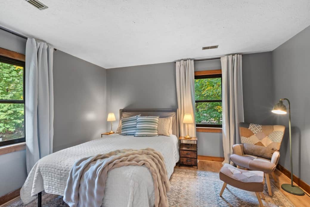 Bright and calming queen bedroom with soft natural tones, plush bedding, and a cozy chair perfect for reading or relaxing.