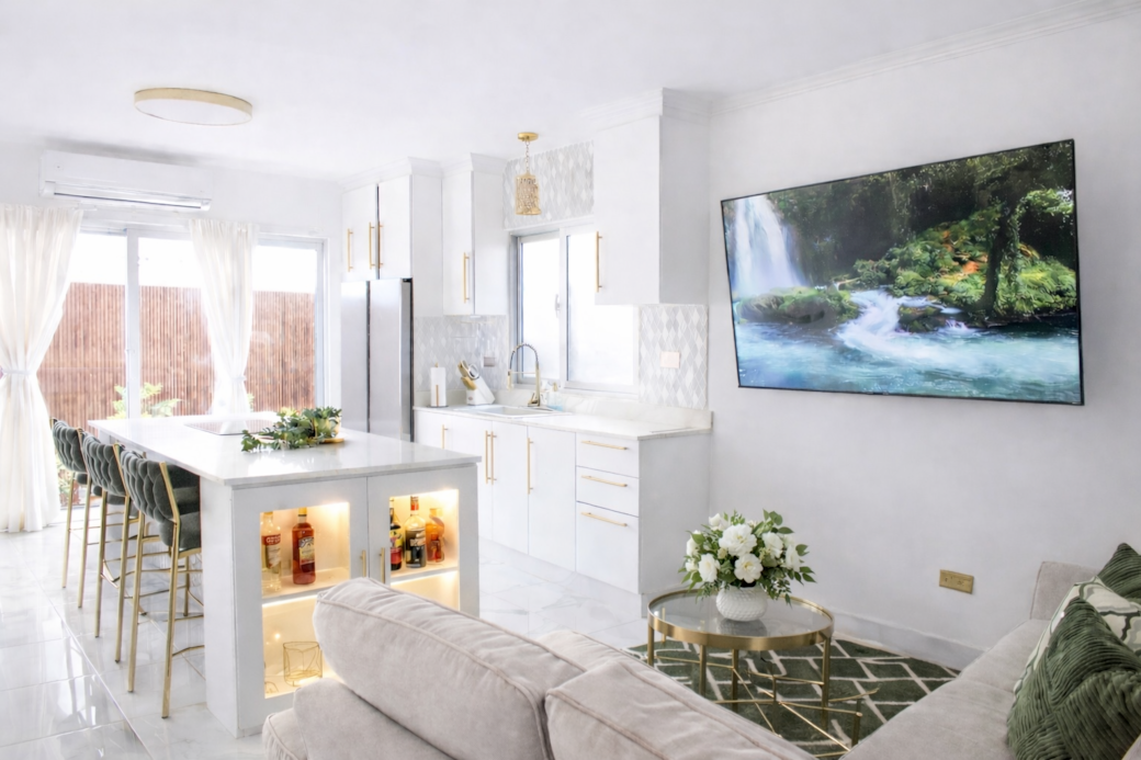 Bright modern kitchen and lounge with island seating, TV, and natural light. Bright modern kitchen and lounge with island seating, TV, and natural light.