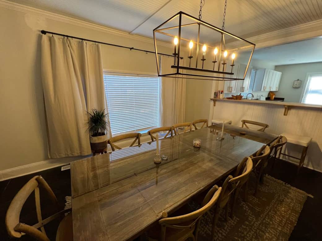 This elegant dining area features a table with six comfortable chairs, perfect for family meals or dinner parties. The space is beautifully lit with six overhead bulbs, and the large window offers a lovely view while you dine.