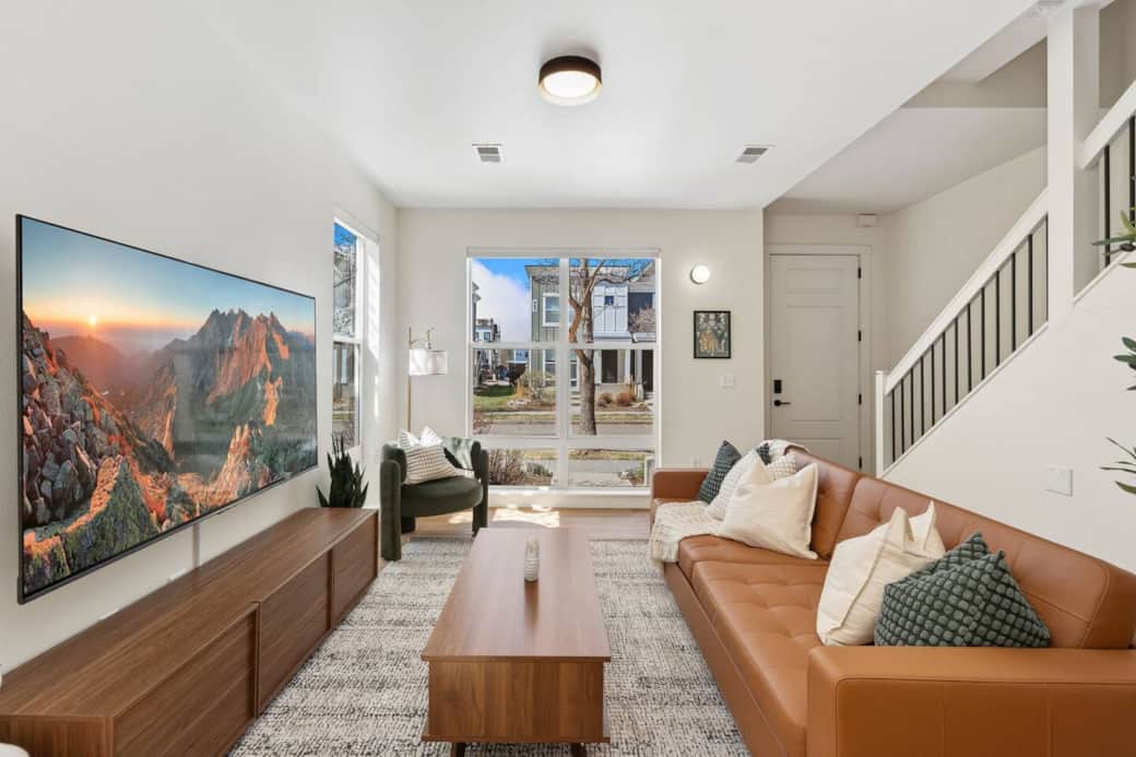 Bright, sun-filled living room with warm modern design, a plush leather sofa, and a large smart TV—perfect for unwinding after a day out or settling in for a relaxed evening at home.
