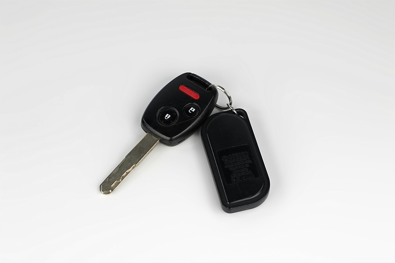 Llave de coche con botones de control y un control negro de alarma sobre fondo blanco