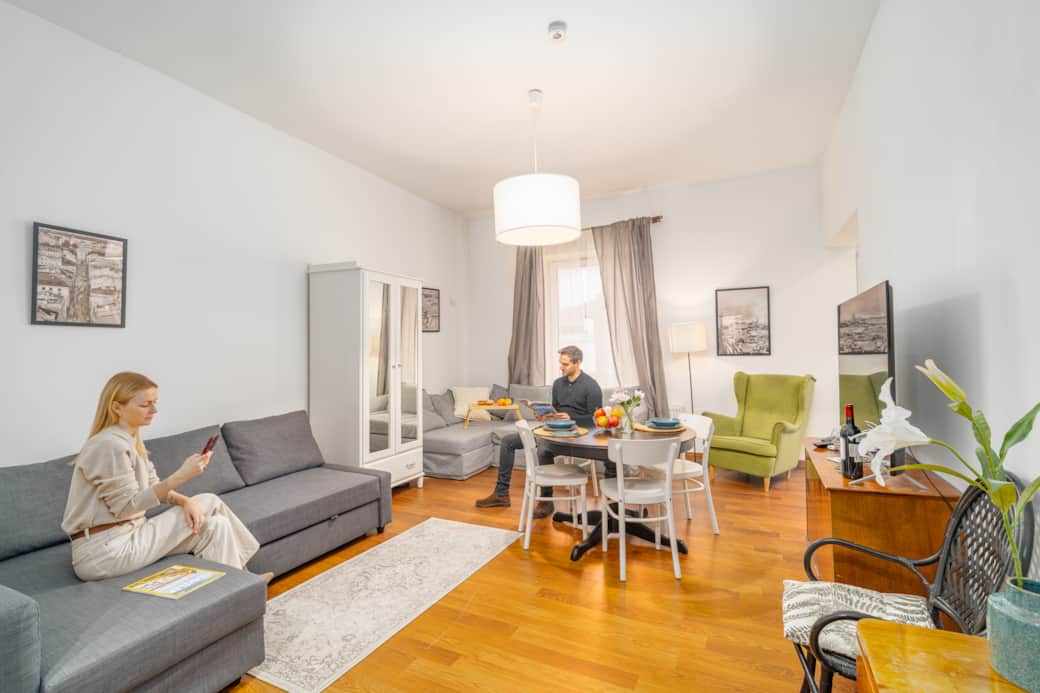 Przestronny, jasny salon z drewnianą podłogą, szarą sofą i narożnikiem.