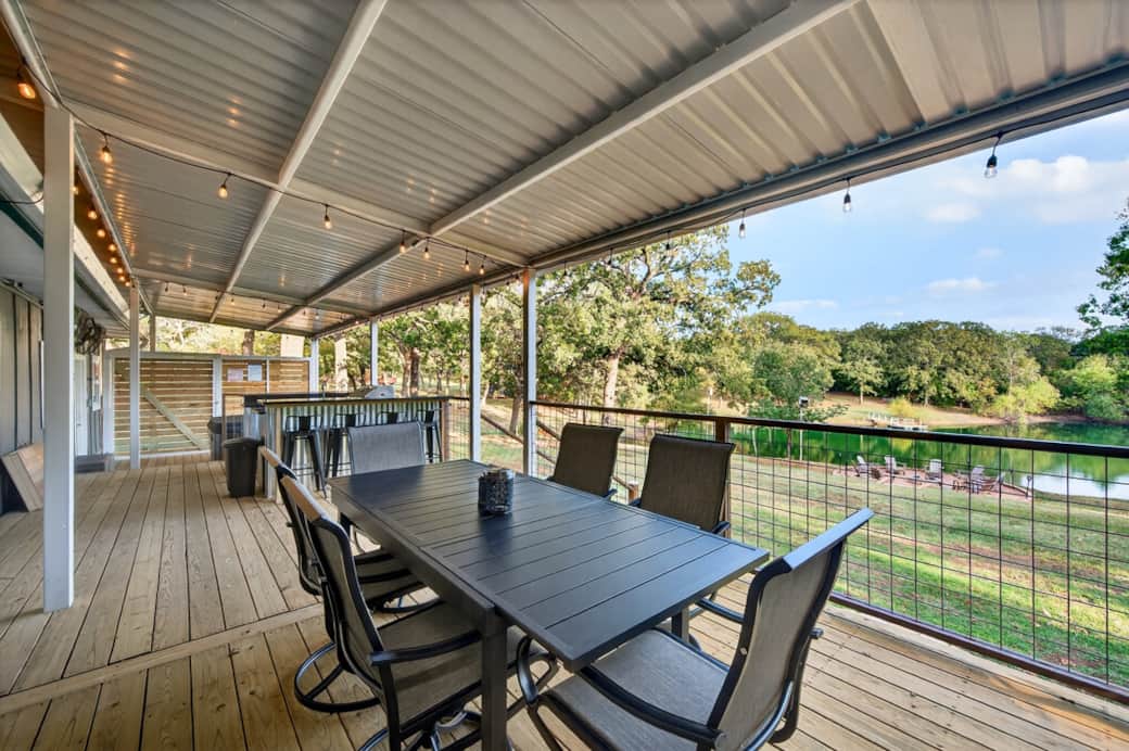 Expansive covered deck with outdoor kitchen, dining area, and peaceful pond views