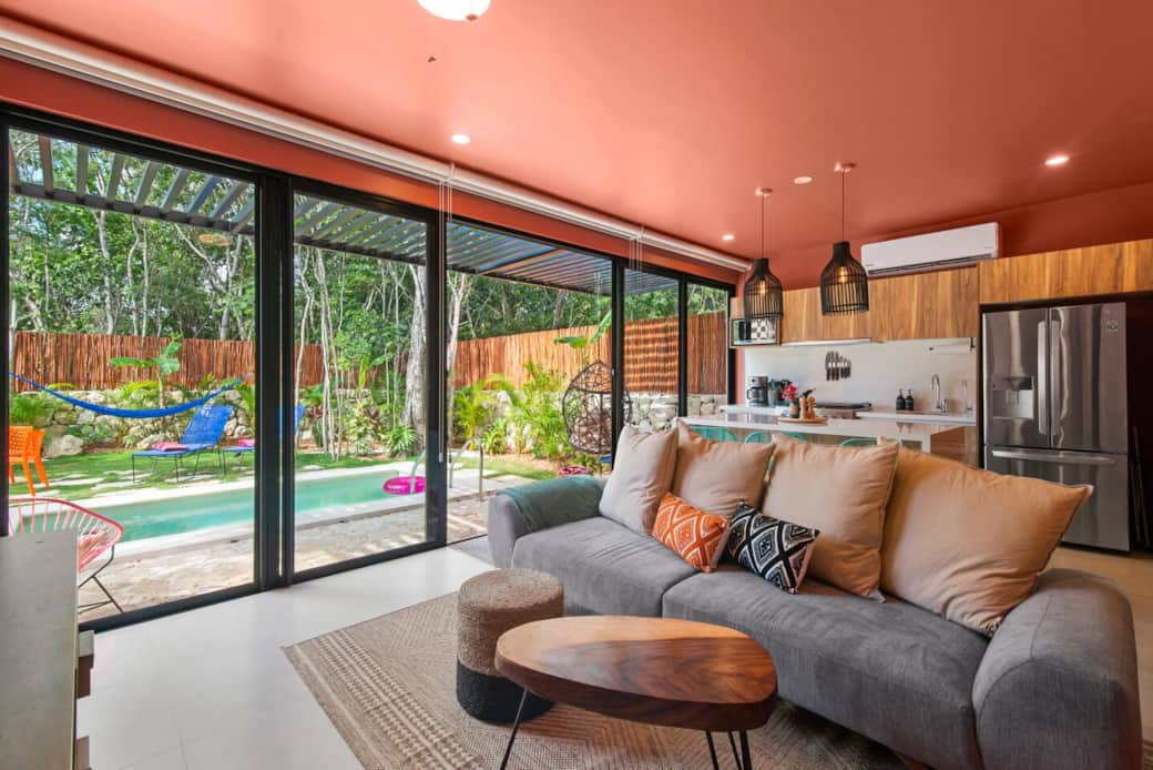 Open-concept living room with A/C, room-darkening shades, and direct access to the backyard and pool with loungers, a hanging chair, hammock, BBQ grill, and outdoor dining table. Includes books and games, plus a 65-inch smart TV.