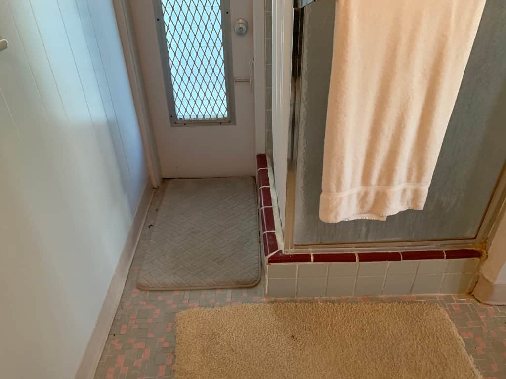 Unit 3 bathroom at Casa Citron before renovation, showing the original shower and a small door leading to the covered patio, highlighting limited access.