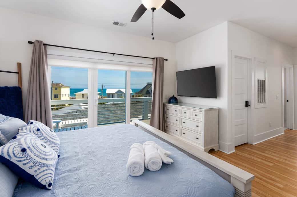 Spacious bedroom with natural light, Smart TV, and sliding doors to outdoor seating with Ocean views.