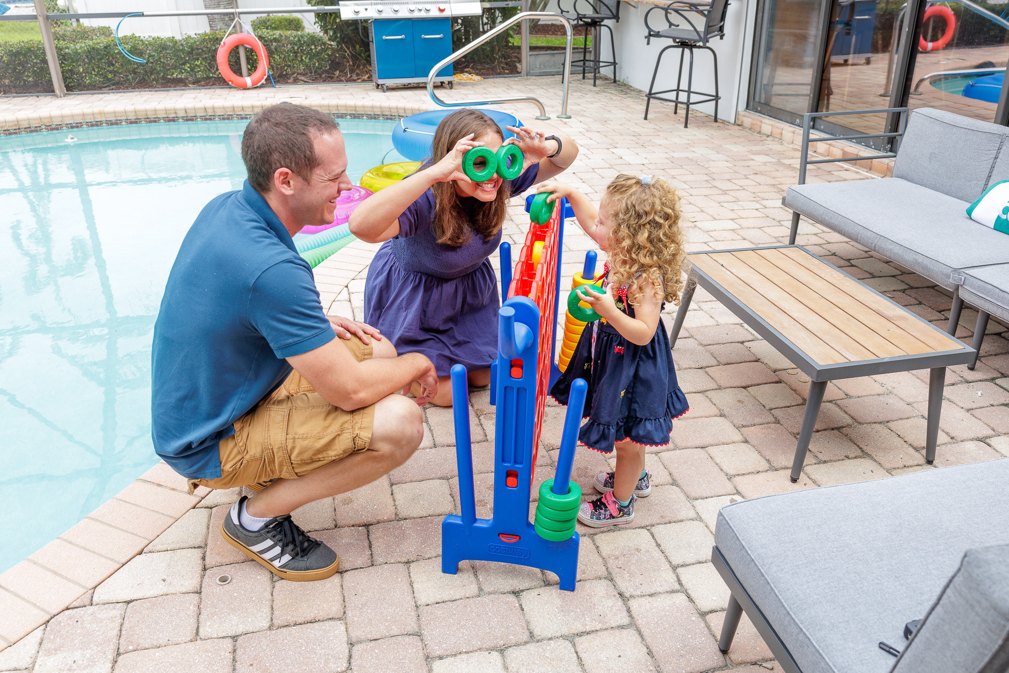 Poolside playtime with family games, lounge seating, and a grill nearby.