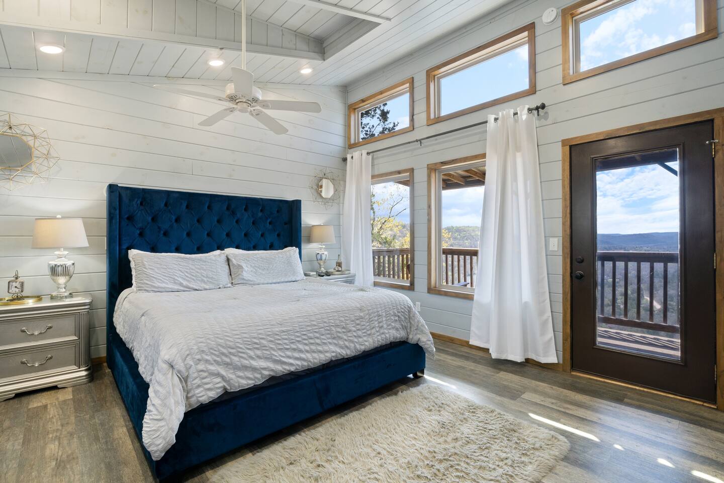 A wide shot of a bedroom with a blue bed, white shiplap walls, and wood floors.