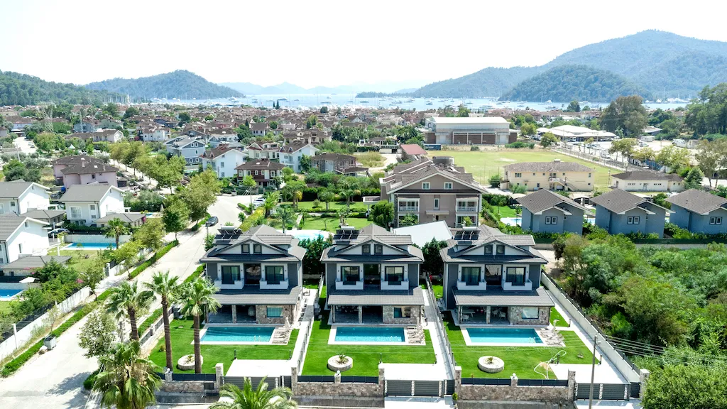 Aerial view of Villa Palmiye B with three houses and swimming pools, surrounded by greenery in Göcek.