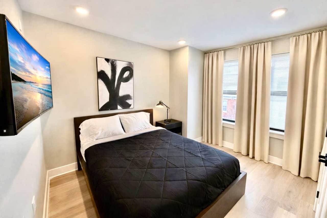 This modern bedroom features a comfortable queen-size bed, a large closet for extended stays, and a w flat-screen TV. Designed with a clean, contemporary style, the room offers a calm and comfortable space to relax, work, or unwind after a long day.
