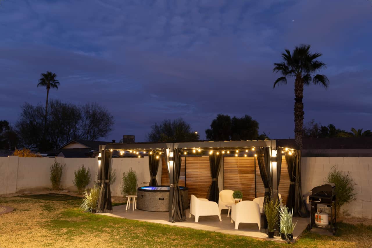 Private hot tub beneath a lighted pergola, with seating alongside.