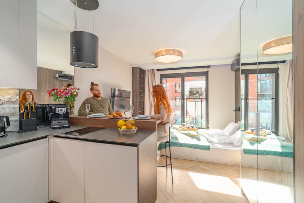 Nowoczesne studio z jasną częścią sypialnianą, dużymi oknami i funkcjonalnym aneksem kuchennym.