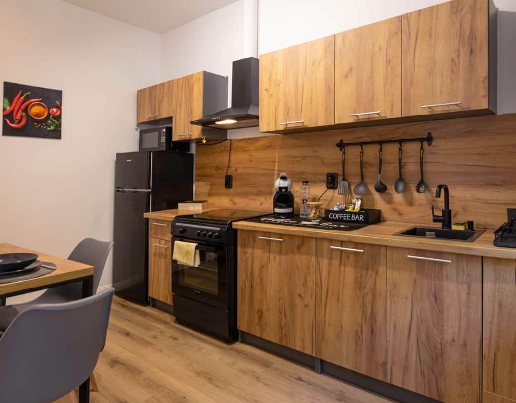 Modern full kitchen with warm wood cabinets, gas stove, full-size fridge, coffee bar, and utensils.