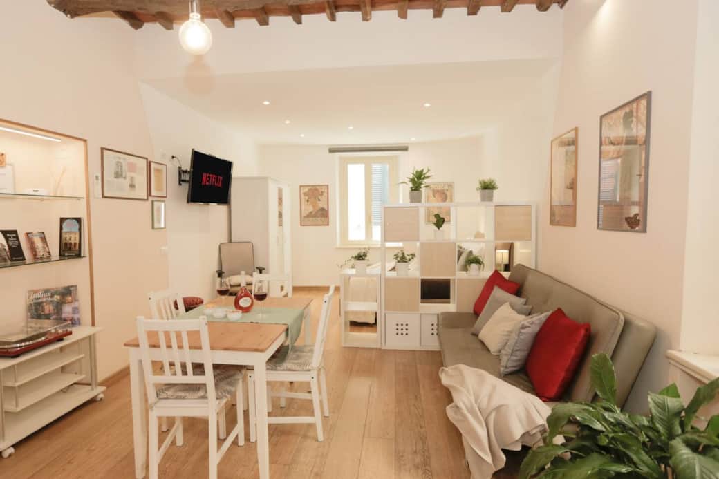 Luminoso salotto con comodo divano, tavolo da pranzo con sedie e TV a schermo piatto. Un elegante separè garantisce privacy dalla zona notte. Ambiente accogliente e funzionale, perfetto per rilassarsi o lavorare in tranquillità.