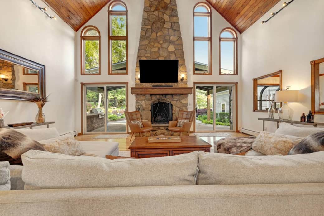 Relax in the elegant living room featuring a vaulted ceiling, grand stone fireplace, and cozy seating. Warm and inviting, it's the perfect space to unwind, connect, and enjoy the morning and evening passing of deer alongside the property.