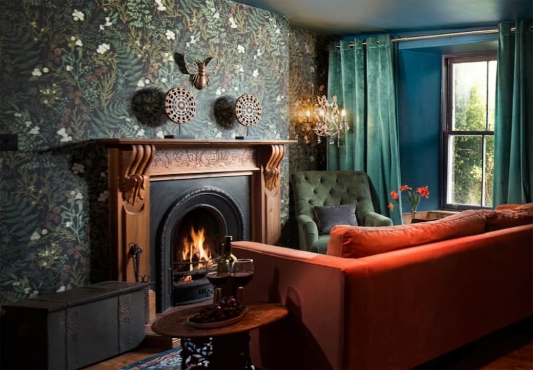 Eccentric Caterpillar lounge: Teal/blue walls, velvet sofa, fireplace, and cozy reading nook.