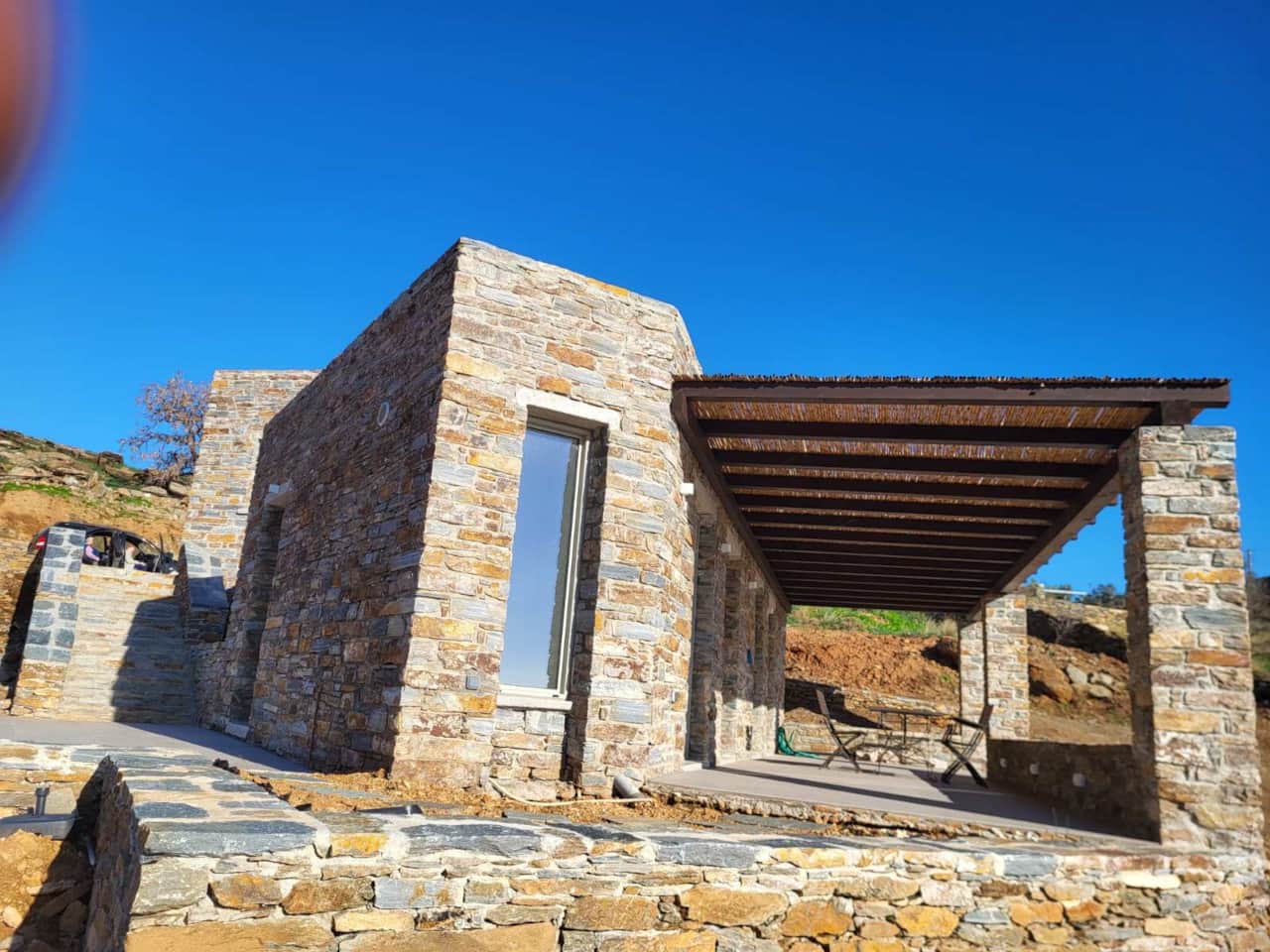 Stone lodging exterior with wooden pergola and blue sky, Koundouros, Kea