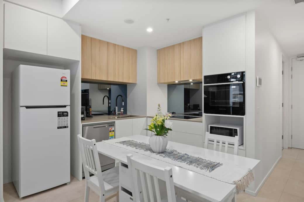 This kitchen and dining area are a harmonious blend of functionality and style. The white refrigerator and oven are ready for your culinary creations, while the dining table, set for four，invites you to enjoy meals in a warm and inviting atmosphere.