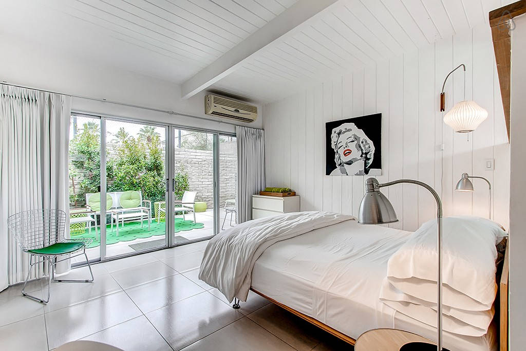 A white bedroom with a bed, two lamps, a chair, and sliding doors leading to a patio.