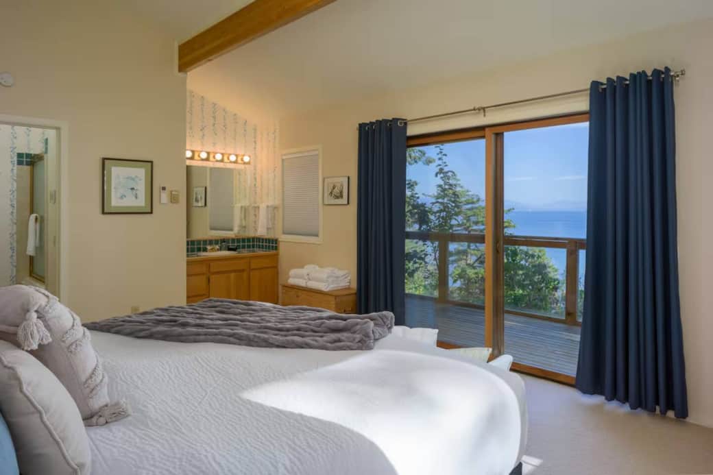 Spacious primary suite featuring a comfortable bed, private ensuite bathroom, and sliding doors that open to stunning water views. Spacious primary suite featuring a comfortable bed, private ensuite bathroom, and sliding doors that open to stunning water views.