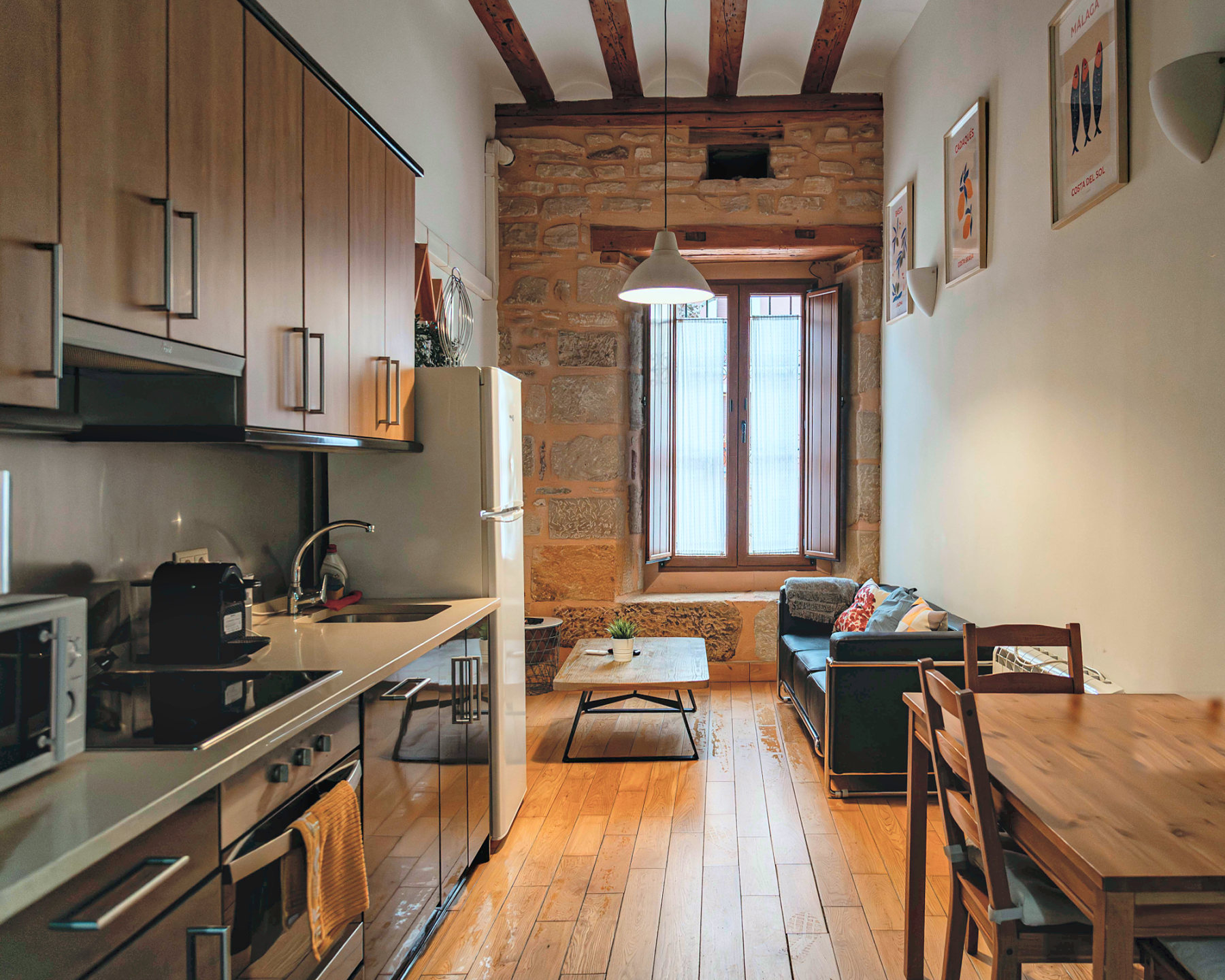 Estudio con cocina, muro de piedra y vigas de madera