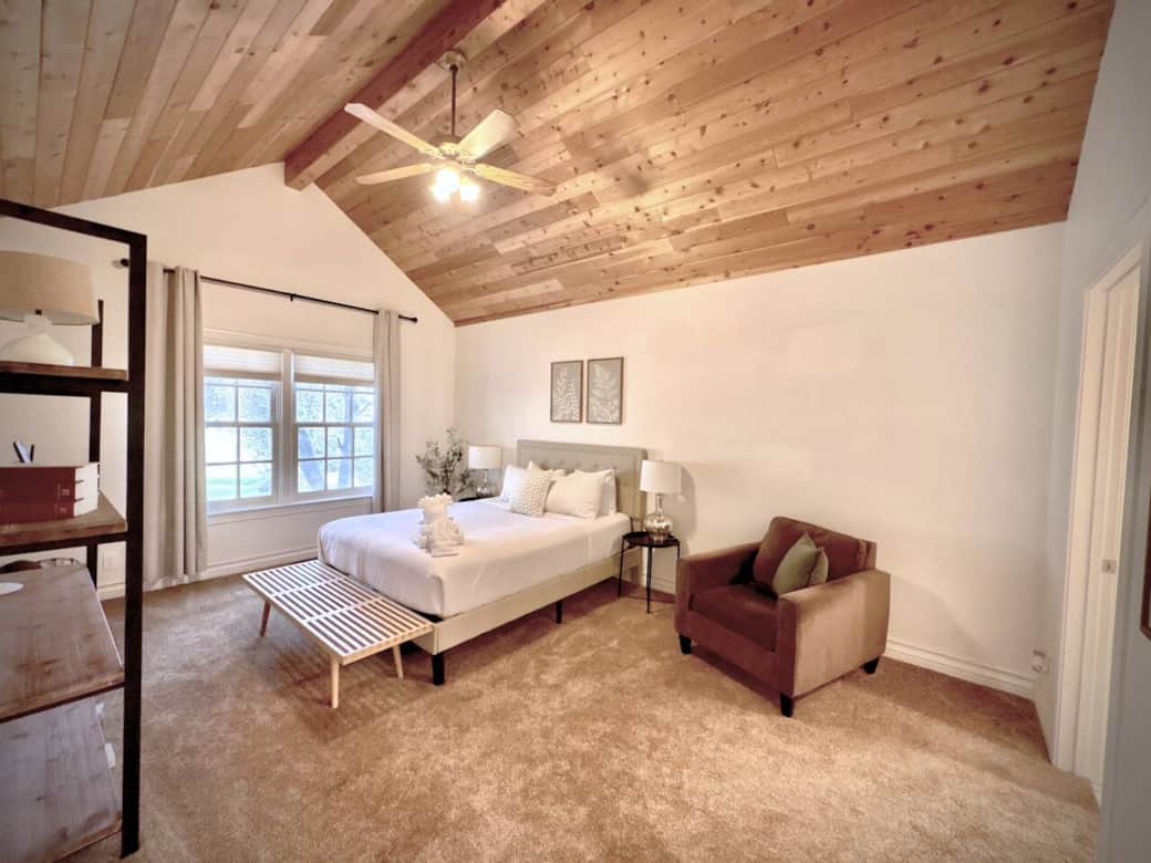 Main Floor Master Bedroom (King Bed) topped by a natural pine ceiling. Artwork and large windows create a peaceful retreat, complete with plush carpeting. With an ensuite bathroom.
